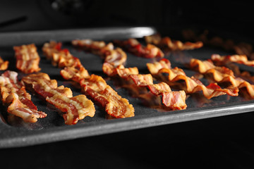 Baking tray with strips of bacon cooking in oven