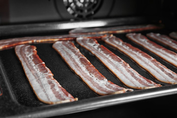 Baking tray with strips of bacon cooking in oven