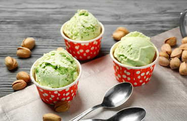Tasty pistachio ice-cream in cups and nuts on wooden background