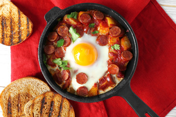 Frying pan with tasty cooked egg and sausages on table
