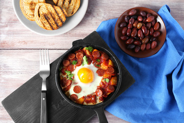 Frying pan with tasty cooked egg and sausages on table