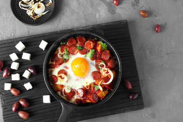 Frying pan with tasty cooked egg and sausages on table