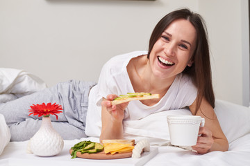 Woman eating sandwich with avocado in bed