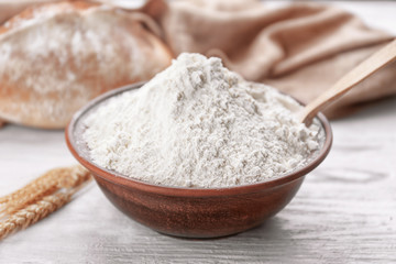 Fototapeta na wymiar Bowl of white flour, bread and wheat ears on wooden table