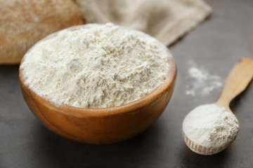 Bowl and wooden spoon full of white flour on grey background