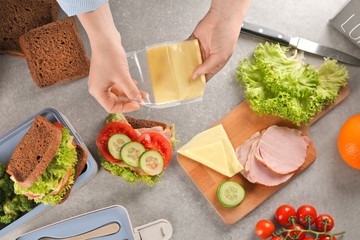 Mother preparing sandwich for school lunch on table