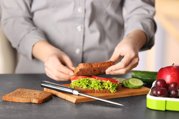 Mother preparing sandwich for school lunch on table
