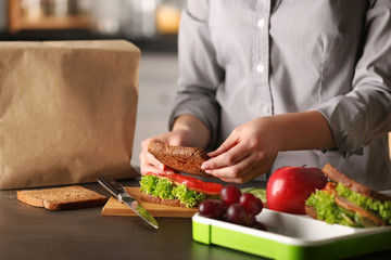 Mother preparing sandwich for school lunch on table