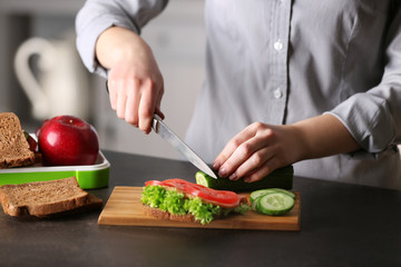 Mother preparing sandwich for school lunch on table