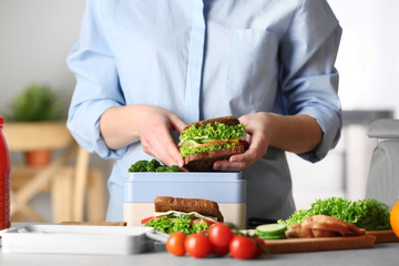 Mother packing meal for school lunch on table