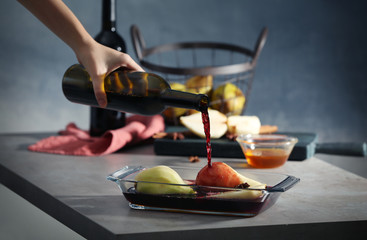Female hand pouring red wine on sliced pear in glass dish