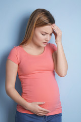 Pregnant woman suffering from headaches on blue background
