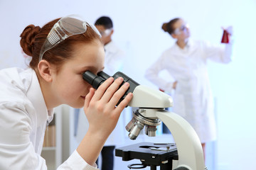 Fototapeta na wymiar Beautiful school girl looking through microscope in chemistry class