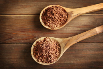 Two spoons with cocoa powder on wooden background