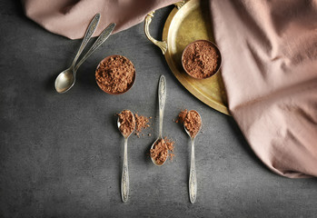 Metal spoons and bowls with cocoa powder on grunge background