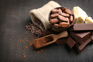 Broken chocolate pieces, cocoa beans and scoop with powder on black background