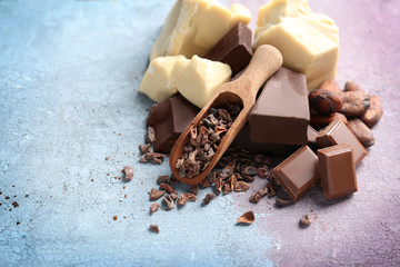 Cocoa nibs in wooden scoop and broken chocolate pieces on light background