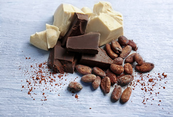 Broken chocolate pieces and cocoa beans on color background