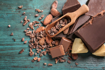 Broken chocolate pieces and cocoa nibs in scoop on color background
