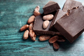 Broken chocolate pieces and cocoa beans on color background