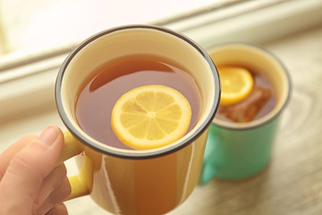 Female hand holding cup of hot tea with lemon, closeup