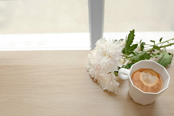 Cup of hot tea and flowers on table near window