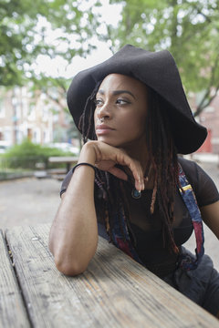 Thoughtful young woman in black hat sitting outdoors