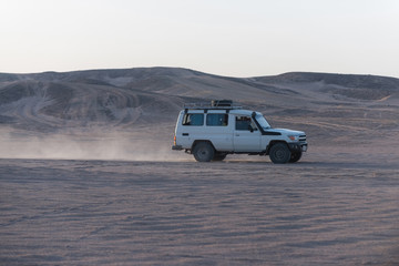 Fototapeta na wymiar White jeep car driving on desert surface in sand dune