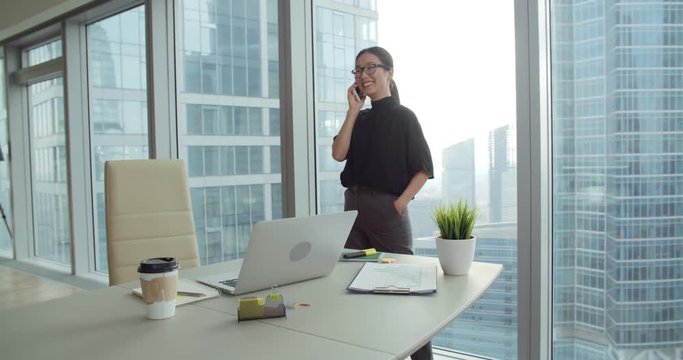 Asian girl busy talking on the phone walks in a modern office,the business situation around