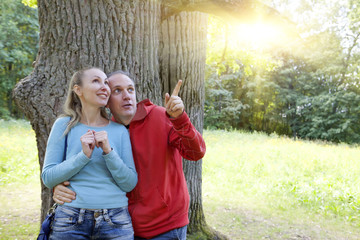 man and  woman near an oak in summer  day have seen something above on a branch and look with a smile..