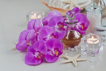 Composition of spa treatment with perfume or aromatic oil bottle surrounded by purple orchids flowers.