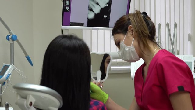 Patient is looking in the mirror while dentist is explaining treatment. Young female dentist is examining a patient. Shot in 4k