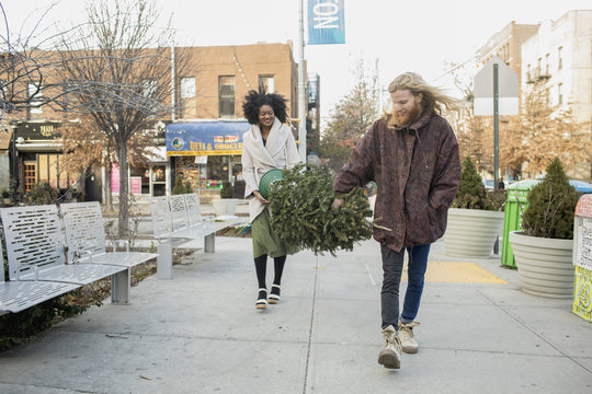 Smiling young couple carrying Christmas tree on footpath