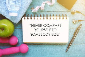 Fitness motivation quotes written on open notebook. Fitness equipment on wooden background.