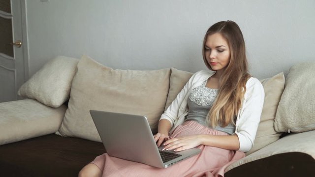 Young woman sitting on couch using laptop and smiling
