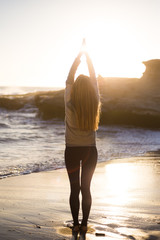 Fototapeta na wymiar Blonde young woman doing yoga on the beach. Girl in black yoga pans, leggins and white sweater. San Diego, California