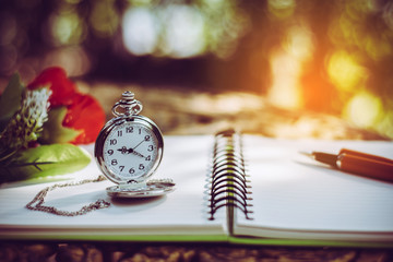 pen, packet watch and rose  on the desk, open a blank white notebook on table