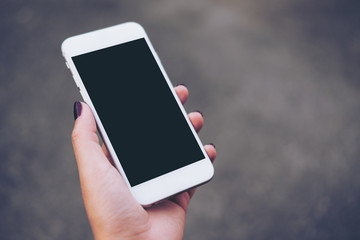 Mockup image of hand holding white mobile phone with blank black screen with blur gray color background 