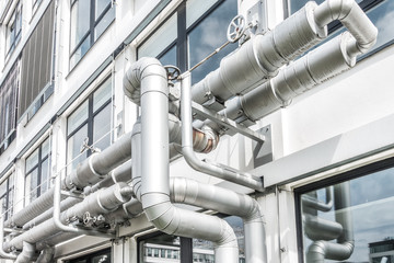 Rohre einer L&uuml;ftungsanlage mit Ventilen an einer Geb&auml;udefassade 