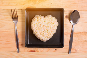 brown rice heart shape on black plate on wooden background