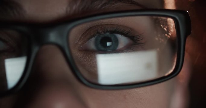 woman with glasses eyes looking at the monitor, surfing the Internet, extreme close-up, dark room