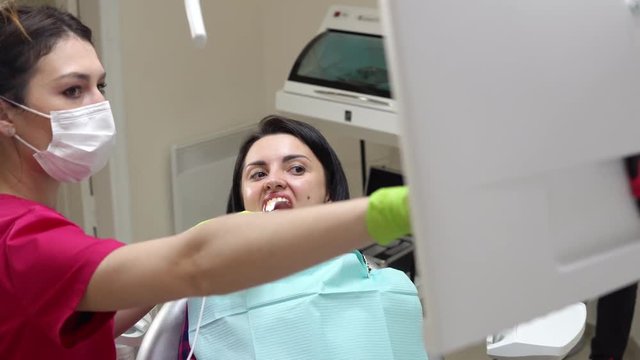 Young female dentist examining the mouth of a patient with an intraoral camera and showing image on the screen explaining to the patient the result of the examination. Shot in 4k