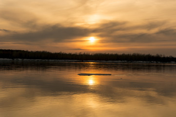 Obraz premium Orange sunset on the river bank. Reflection of the sunset in the water. The ice floes on the water.