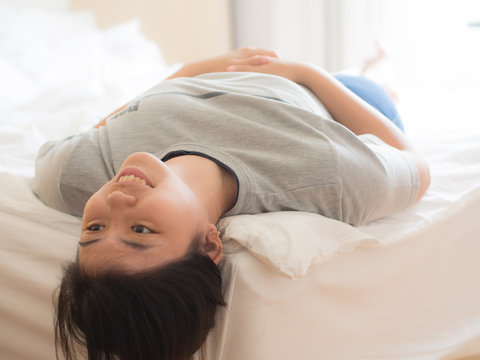 smiling young chinese woman lying upside down on the bed