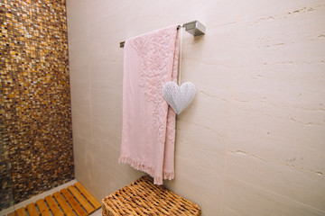 A pink towel is dried in the bathroom on the heated towel rail. White heart, an element of decor. Wicker basket for clothes.