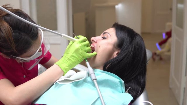 Woman at the dental hygienist getting professional tooth whitening and ultrasound cleaning. Dentist using saliva ejector or dental pump to evacuate saliva. Shot in 4k