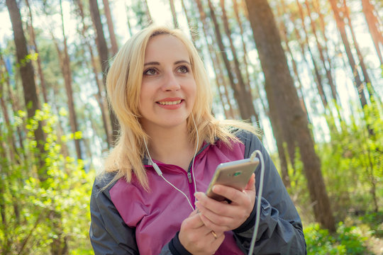 a sports girl holding the phone and listening to music after a run in the woods. The concept of a healthy lifestyle