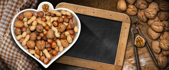 Dried fruits in a bowl in the shape of a heart on a table with a blackboard - Healthy eating - obrazy, fototapety, plakaty