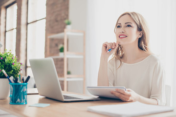 Portrait of young beautiful thoughtful lady sitting at the table working with laptop on writing down new ideas