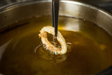 Lightly fried Calamari ring being taken out of a pan of hot oil.